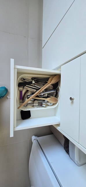 A kitchen cabinet with a drawer containing various utensils and kitchen tools.