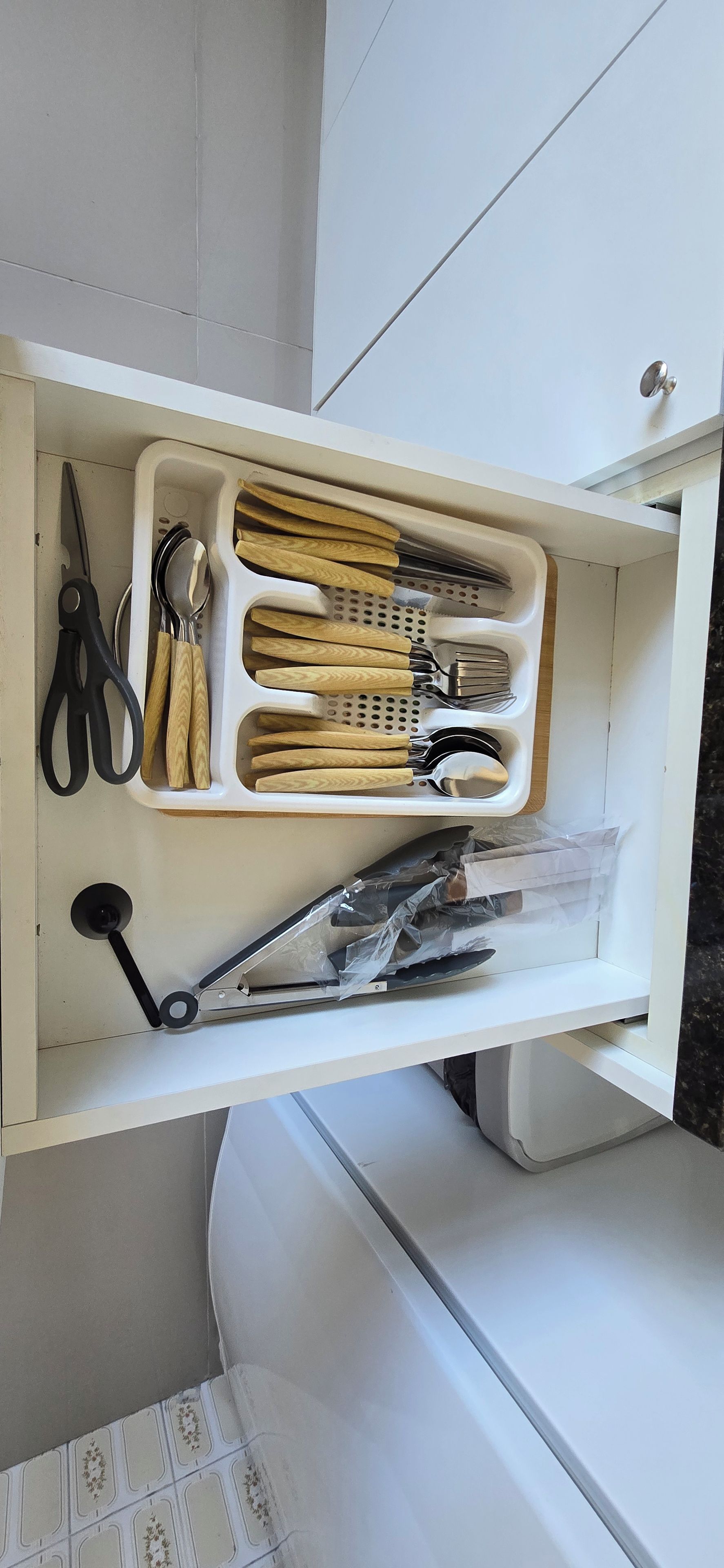Un cajón con varios utensilios de cocina, como unas tijeras, una cuchara y una espátula.