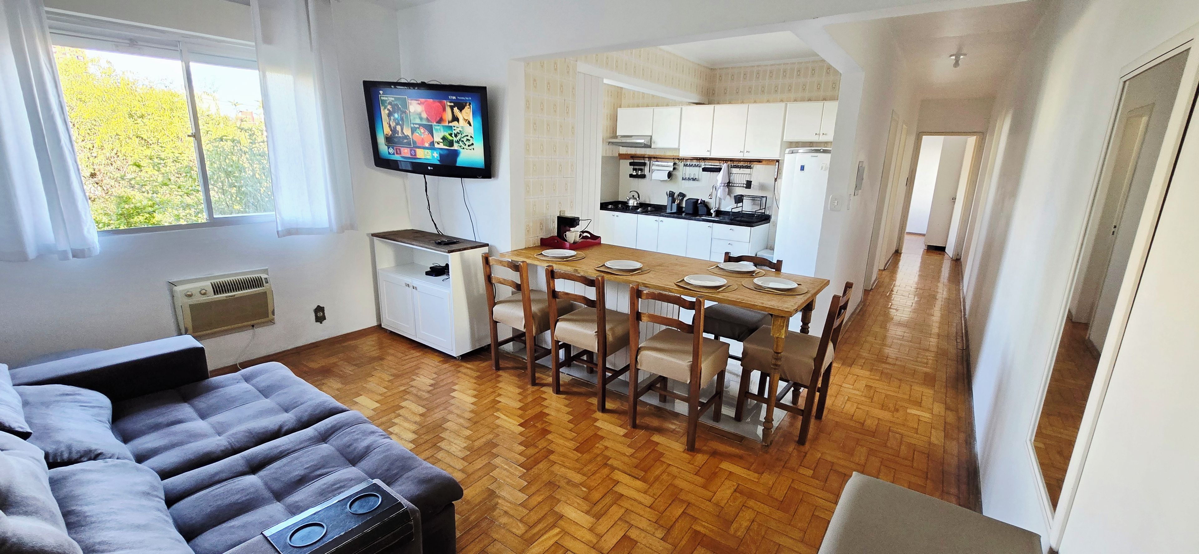 Un espacio habitable compacto con comedor, kitchenette y televisor montado en la pared.