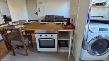 A compact kitchen with a wooden table, chairs, a built-in oven, and a washing machine.