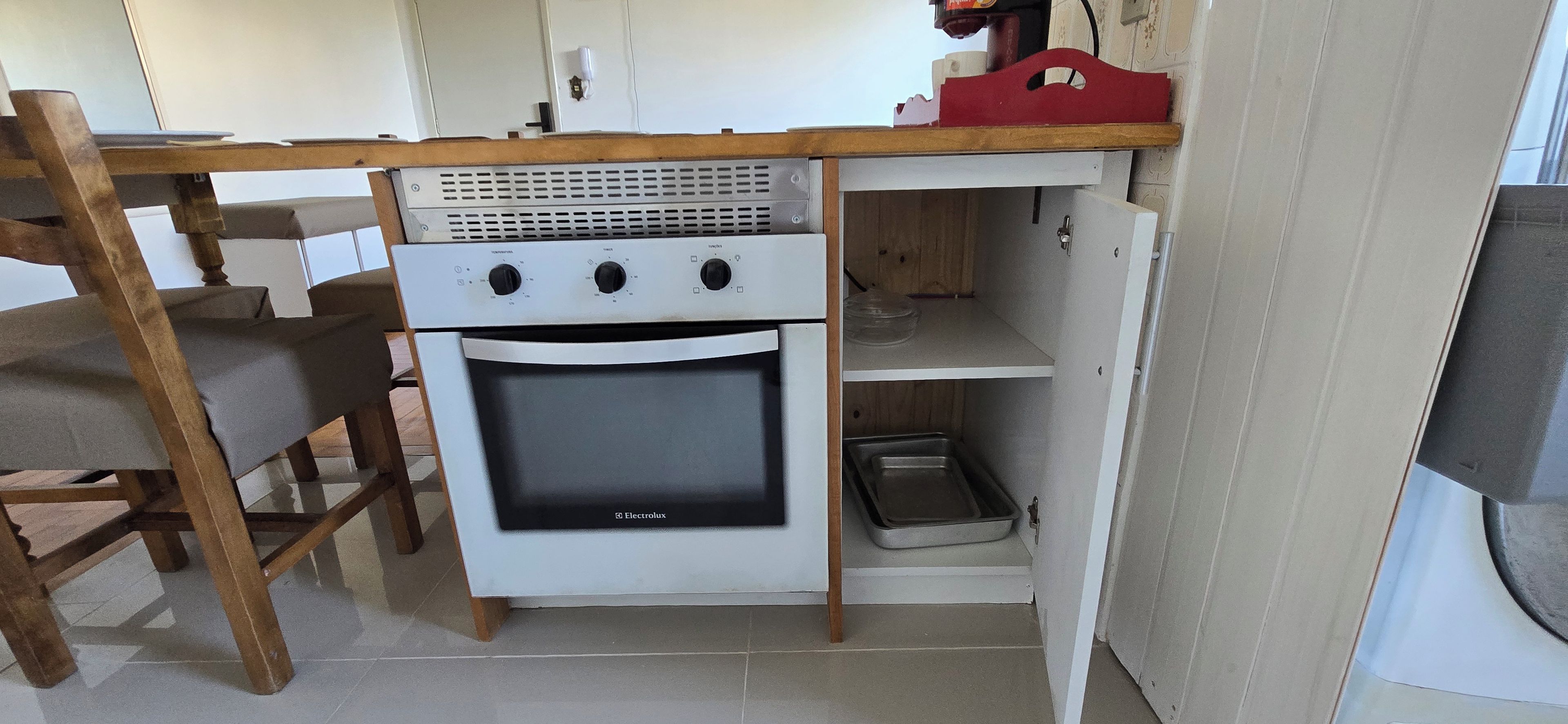 Une cuisine compacte dotée d’un four encastré, d’une table à manger en bois et d’une petite étagère.