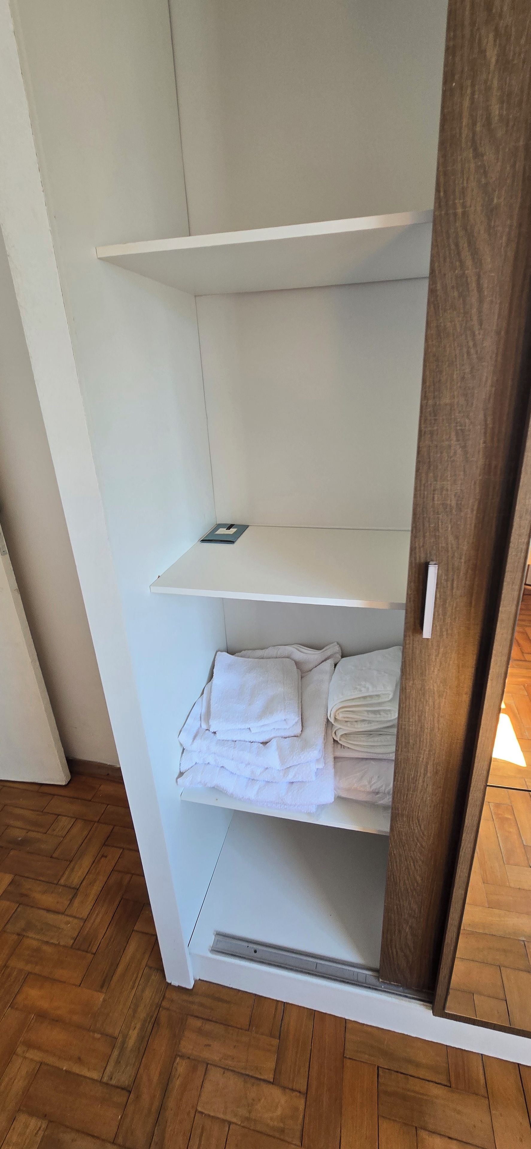 Un armario de madera con la puerta entreabierta, mostrando toallas blancas dobladas y un objeto pequeño en el estante superior.