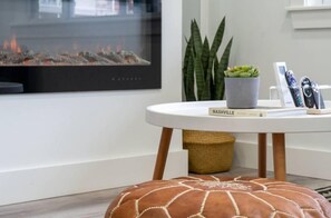 A modern living room with a fireplace, a round white table, a potted plant, and a book titled "Nashville". - Melrose 1BR Getaway with Pool  by Barcle (Nashville)