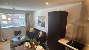 A modern living room with a dining area, a sofa, a painting on the wall, and a kitchen with a stove.