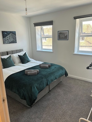 Ein Schlafzimmer mit einem Bett, zwei Fenstern, einem Bild an der Wand und einer Deckenleuchte.