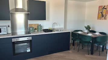 A modern kitchen with built-in appliances, a dining area with green chairs, and a painting on the wall.