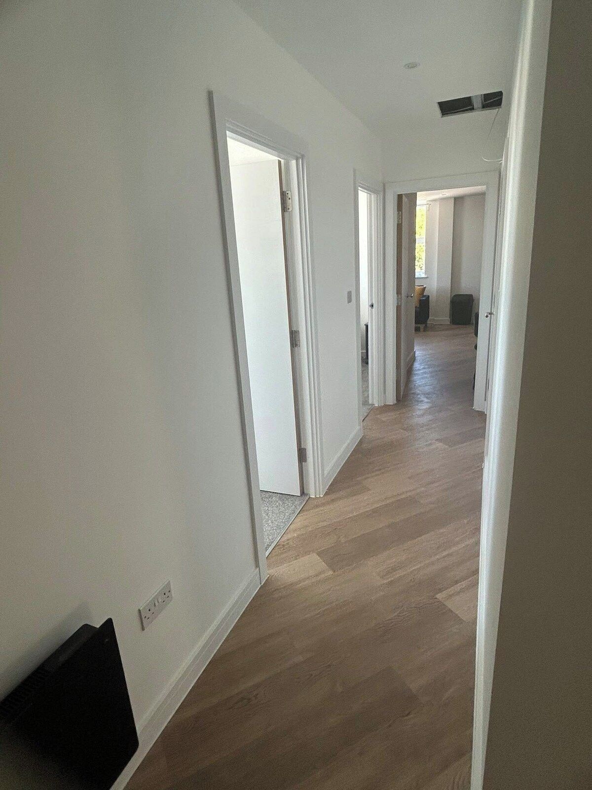 A hallway with wooden flooring and white walls, leading to an open living area.