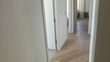 A hallway with wooden flooring and white walls, leading to an open living area.