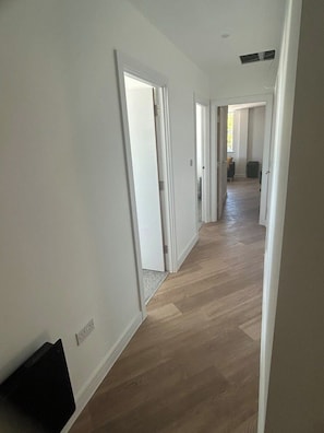 Ein Flur mit Holzboden und weißen Wänden, der in einen offenen Wohnbereich führt.