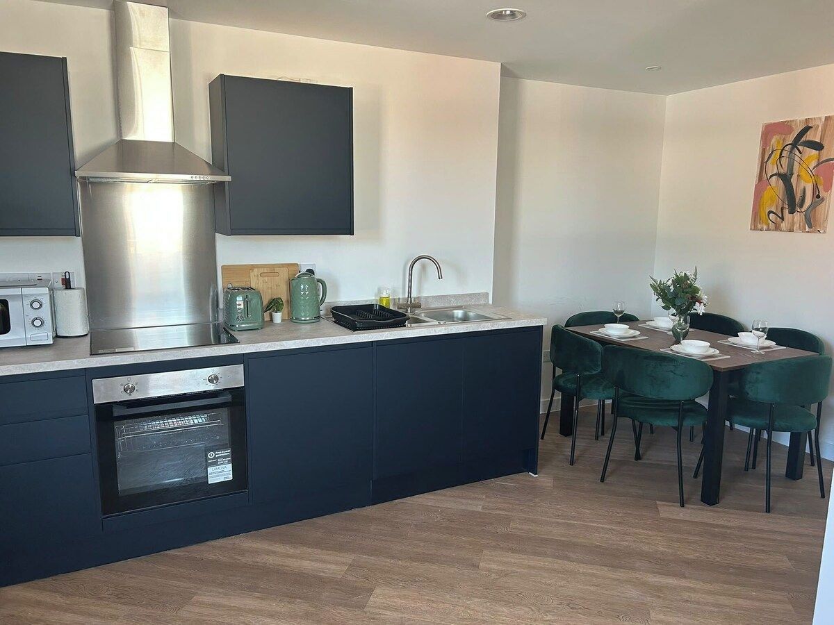 Une cuisine moderne dotée d’appareils électroménagers intégrés, un coin repas avec des chaises vertes et un tableau accroché au mur.