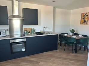 Eine moderne Küche mit eingebauten Geräten, eine Essecke mit grünen Stühlen und ein Gemälde an der Wand.