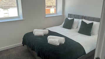 Une chambre à coucher avec un lit, deux fenêtres, un luminaire suspendu et une vue sur l’extérieur.