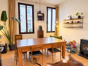 Un coin repas avec une table et des chaises en bois, une cheminée et une vue sur l’extérieur grâce à de grandes fenêtres.