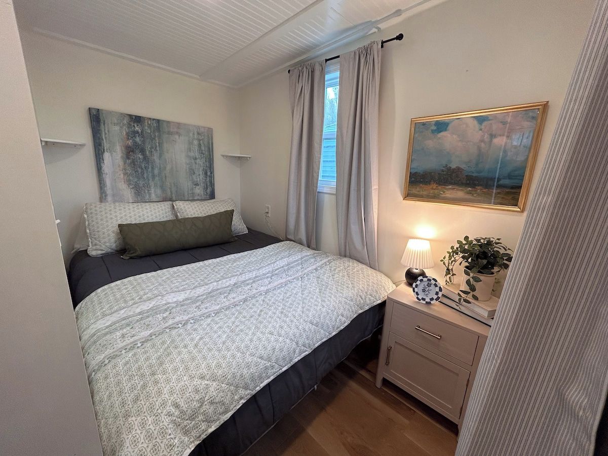Une chambre à coucher avec un lit, une table de chevet, une lampe et une œuvre d’art.