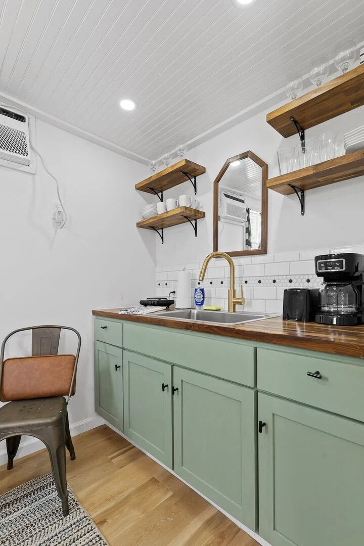 A kitchen with a wooden countertop, a sink, a coffee maker, and green cabinets.