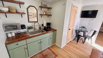 A compact kitchen with a built-in toaster, a sink, and a coffee maker. There is a dining area with a table and chairs, and a TV mounted on the wall.