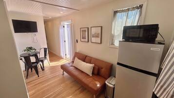A living room with a sofa, a small table with a plant, a TV mounted on the wall, and a refrigerator.