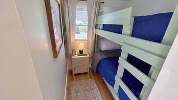 A narrow room with bunk beds, a bedside table with a lamp, and a patterned rug.