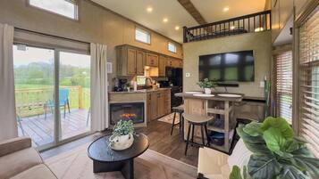 A modern kitchen with a fireplace, a dining area with a round table, and a balcony with a view of the outdoors.