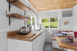 Une cuisine compacte avec un plan de travail en bois, une bouilloire, un four à micro-ondes et un évier. Une fenêtre offre une vue sur la verdure environnante.