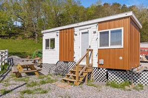 A mobile home with a wooden exterior, a front porch, and a small attached structure. - Quail Run Farm- Rustic Tiny Home 1 (Chattanooga)