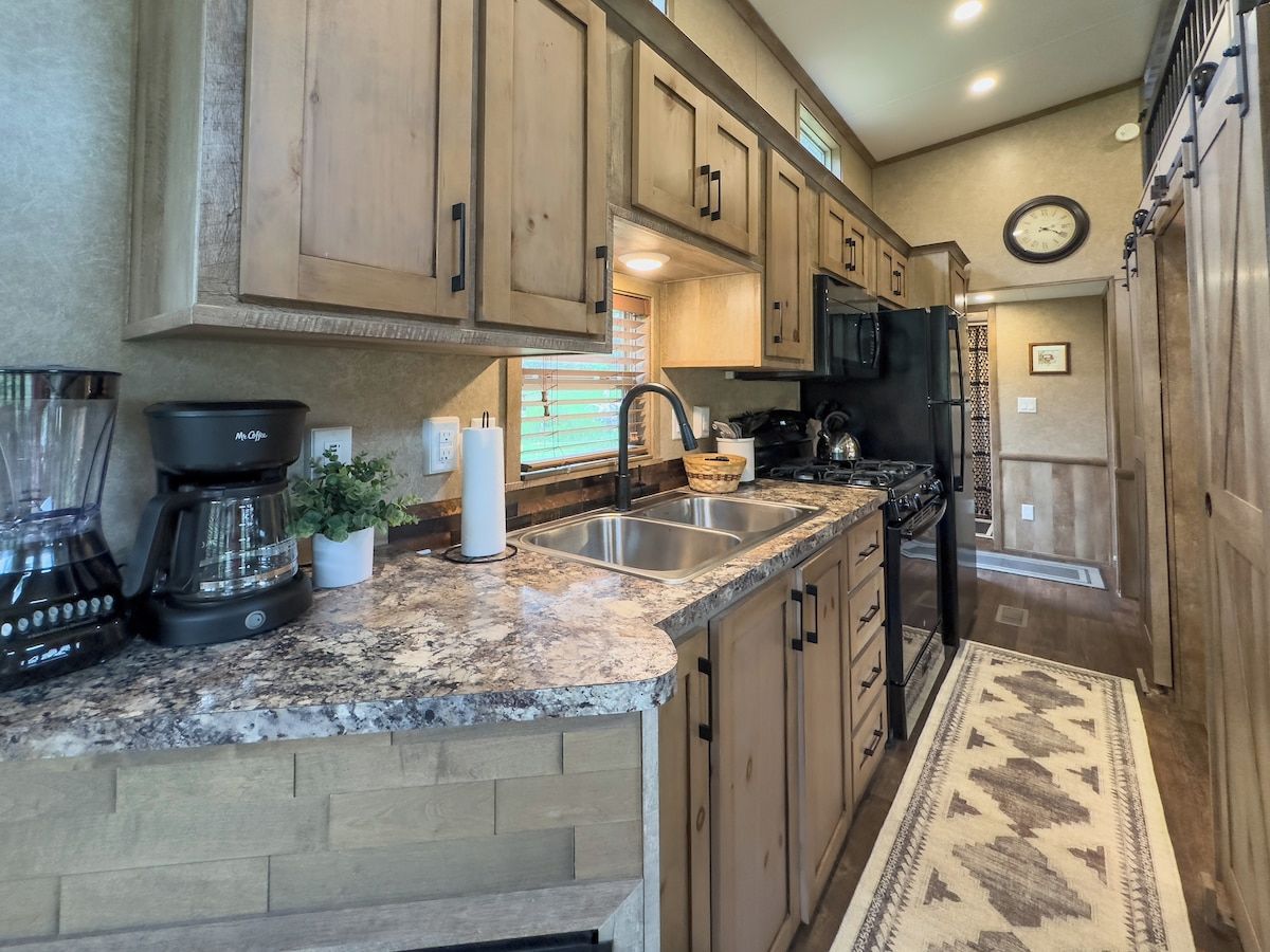 A kitchen with wooden cabinets, granite countertops, a stainless steel sink, and a black stove.