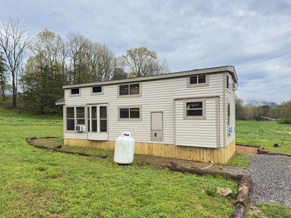 Une maison mobile de plain-pied, dotée d’un porche à l’avant, d’une grande cuve de propane et d’une cour clôturée.