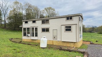 Une maison mobile de plain-pied, dotée d’un porche à l’avant, d’une grande cuve de propane et d’une cour clôturée.