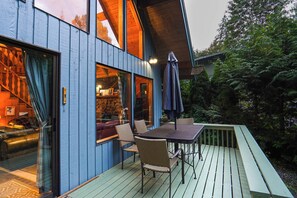 Eine Holzterrasse mit Gartenmöbeln, ein Glastür-Eingang und Blick ins Innere.