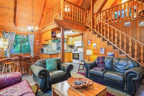 Ein Interieur einer Hütte mit zwei Ledersofas, einem Essbereich, einer Küche und einer Treppe.