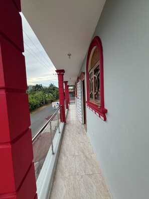Un pasillo con pilares rojos, suelo de baldosas y vista a la calle.
