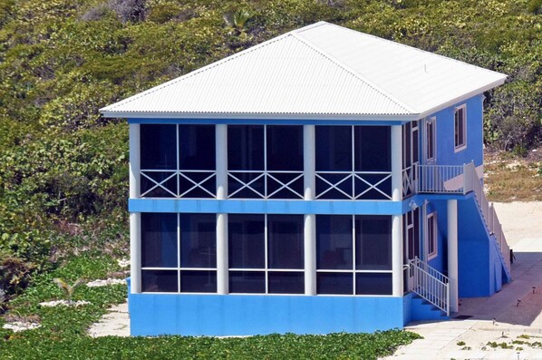 Een gebouw met twee verdiepingen, een wit dak en blauwe buitenmuren, met grote ramen en een balkon op de bovenverdieping.