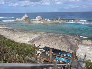 A beachside hut with a thatched roof, a pool, and lounge chairs.