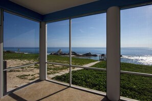 A room with large windows overlooking a beach with rocks and greenery. - Bahama Dreamin' Ocean Front Villa 1/1 (Long Island)