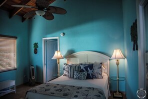 Een slaapkamer met een bed, twee bedlampen, een plafondventilator, een deur en een raam met jaloezieën.