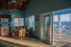 A kitchen with a dining area, a ceiling fan, and a view of the ocean through a glass door. - Blue Up Oceanview Villa – 1 Bed/ 1 Bath Upstairs (Long Island)