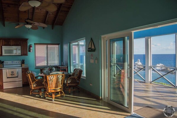 A kitchen with a dining area, a ceiling fan, and a view of the ocean through a glass door.