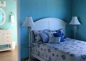 A bedroom with a bed, two bedside lamps, a dresser, and a mirror. - Bahama Dreamin’ Downstairs Oceanfront Villa – 2/2 (Long Island)
