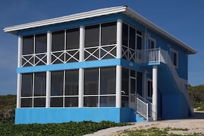 A two-story building with large windows, a balcony, and a staircase leading to the upper floor. - Bahama Dreamin’ Downstairs Oceanfront Villa – 2/2 (Long Island)