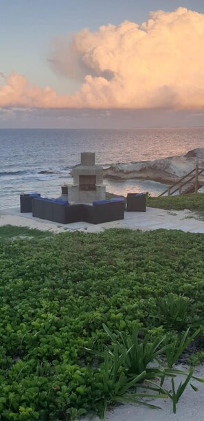 A beachside lounge area with a stone structure, seating, and a view of the ocean. - Bahama Dreamin' Upstairs Oceanfront Villa 2/2 (Long Island)
