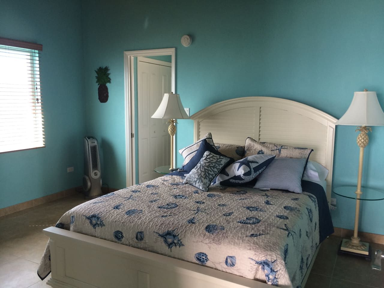 A bedroom with a bed, bedside lamps, a door, and a potted plant.