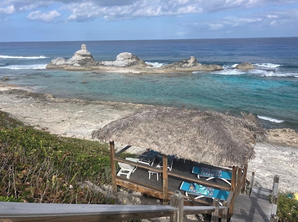 A beachside hut with a thatched roof, a pool, and lounge chairs.