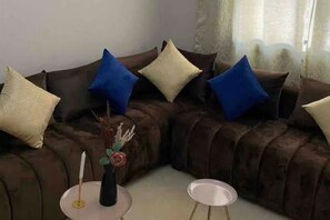 Ein Ecksofa mit vielen Kissen, ein kleiner Tisch mit Kerze und eine Vase mit Trockenblumen.