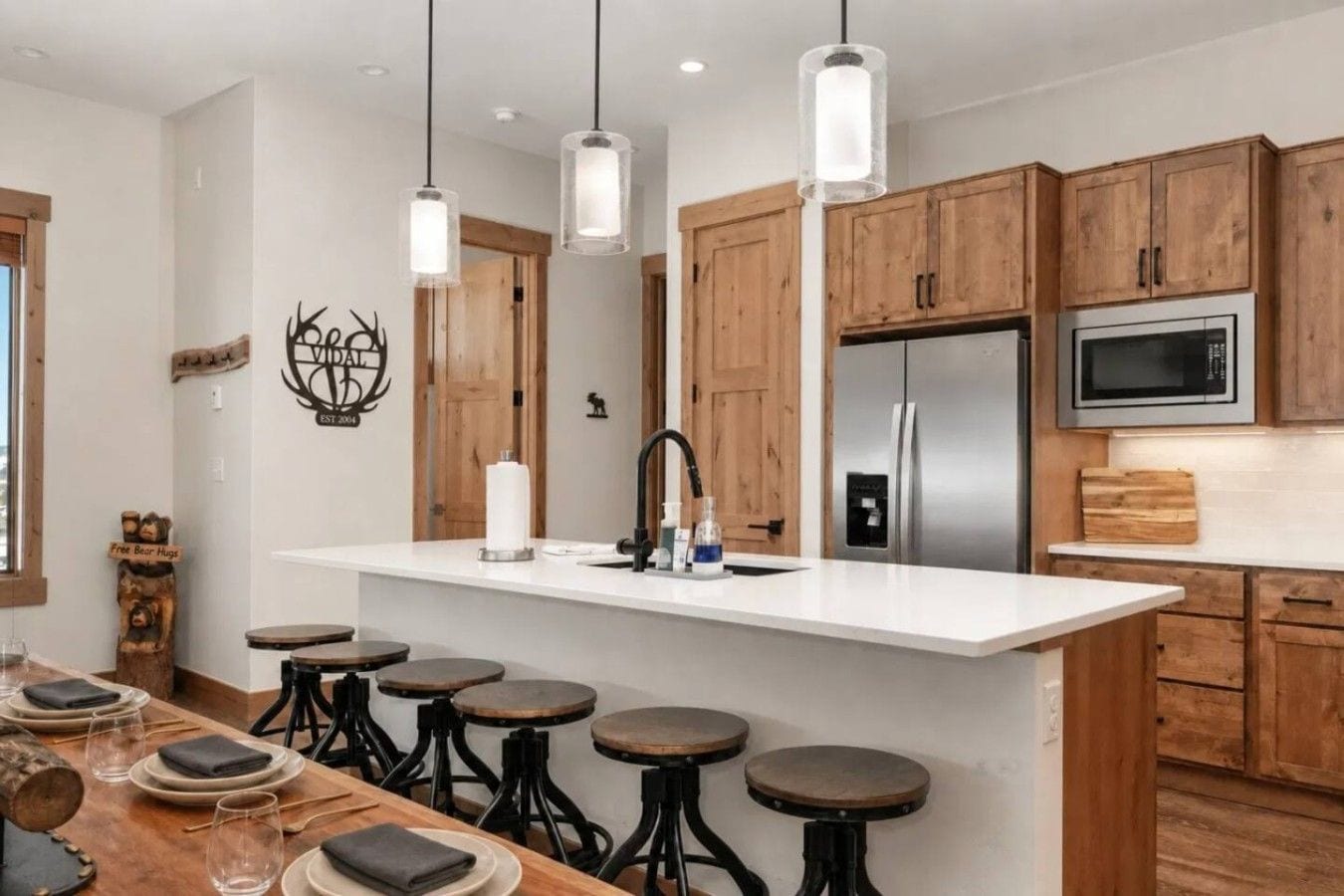 A modern kitchen with wooden cabinets, a stainless steel refrigerator, a microwave, and a bar area with stools.