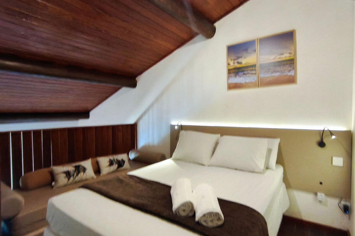 A bedroom with a sloped ceiling, a bed with white linens, a brown headboard, and a painting on the wall.