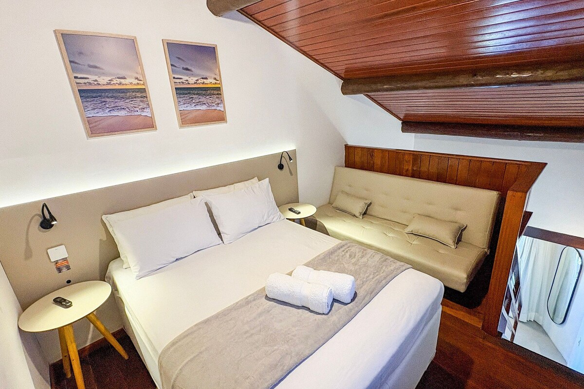 A bedroom with a bed, a sofa, a bedside table, and a wall-mounted lamp.