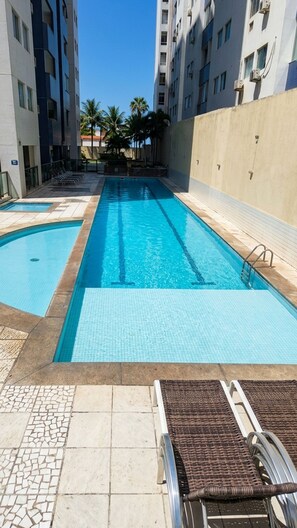 A swimming pool with two separate sections, surrounded by a tiled deck and lounge chairs. - Studio Vista Mar  (Salvador)