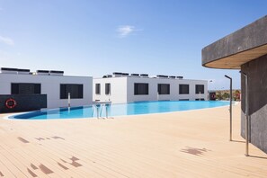 A swimming pool with a wooden deck, a lifebuoy, and a building with a flat roof. - Home2Book Bright Abades Apt, Pool & Gym (Abades)