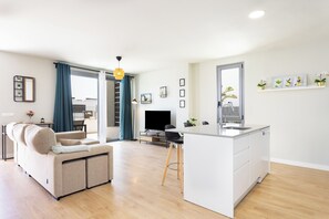 A modern living room with a sofa, a TV, and a kitchen area with a sink and counter. - Home2Book Bright Abades Apt, Pool & Gym (Abades)
