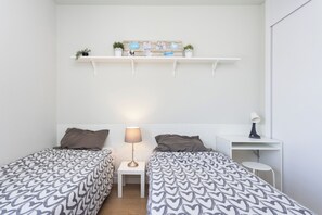 A room with two beds, a small table, a lamp, and a shelf with photos and plants. - Home2Book Bright Abades Apt, Pool & Gym (Abades)